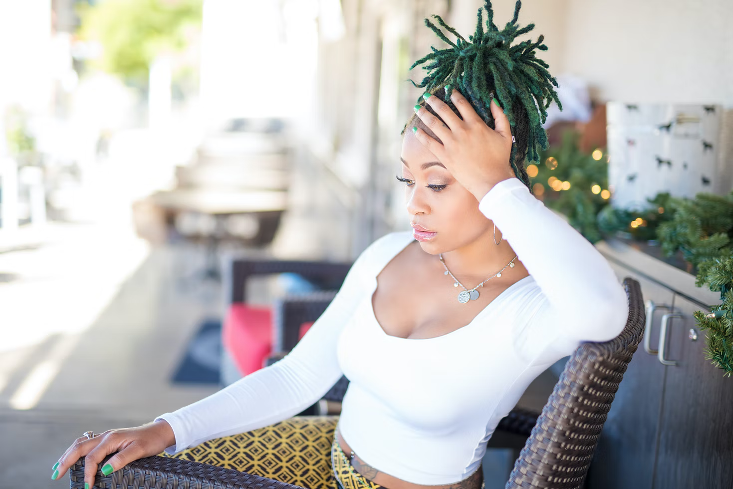 A woman with green dreadlocks sitting on a chair outside.