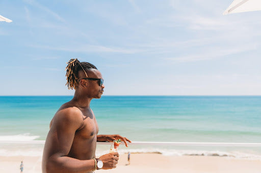 Man with dreadlocks walking along a beach without a shirt.