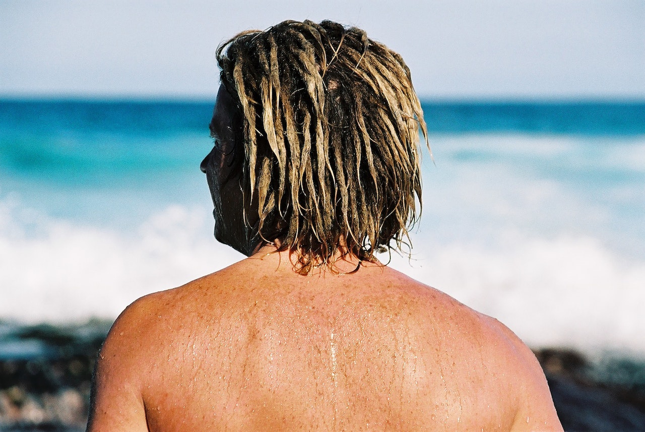 A man with blonde locs in front of a beach