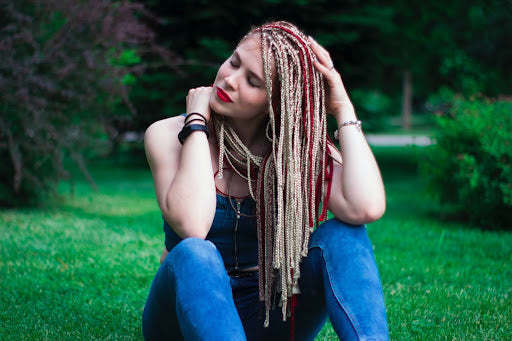 Young woman sitting on grass with dreadlock extensions. 