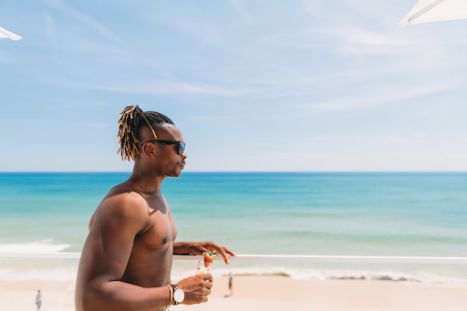 A shirtless man with dreadlocks at the beach.