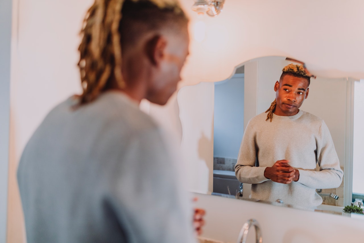 Man with dreadlocks looking at himself in the mirror